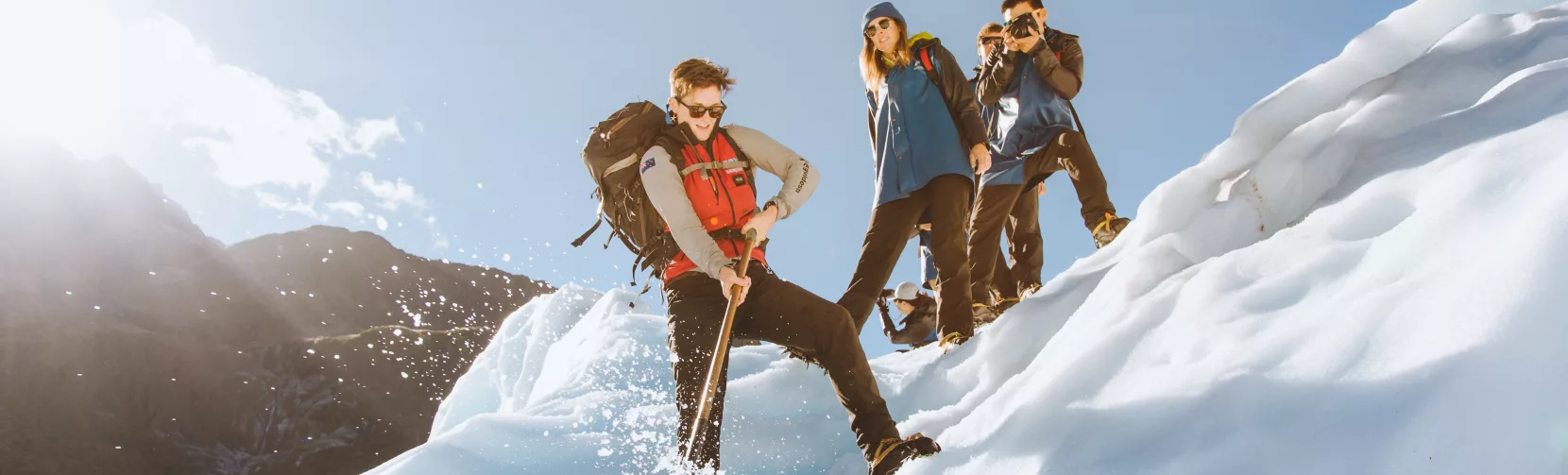 A guide demonstrates ice axe techniques on a slope while hikers look on.