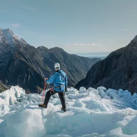 Helihiker standing on Fox Glacier with views of ice formations and alpine valleys on the West Coast