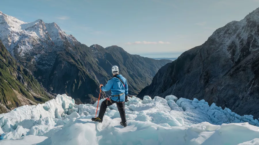 Helihiker standing on Fox Glacier with views of ice formations and alpine valleys on the West Coast