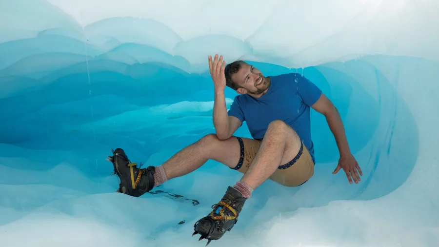 Man exploring a vibrant blue ice cave during an ice caving tour on Fox Glacier, West Coast New Zealand