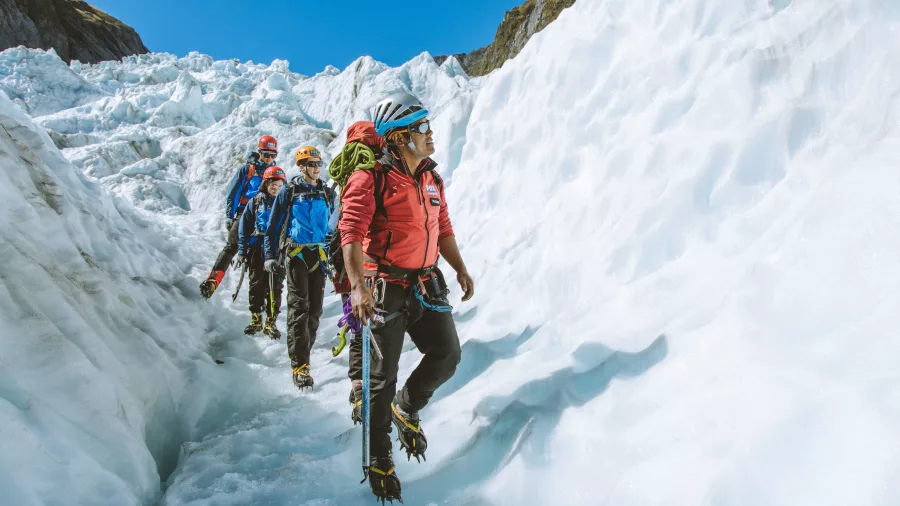 A glacier guide leads a group through a narrow icy passage with climbing gear.