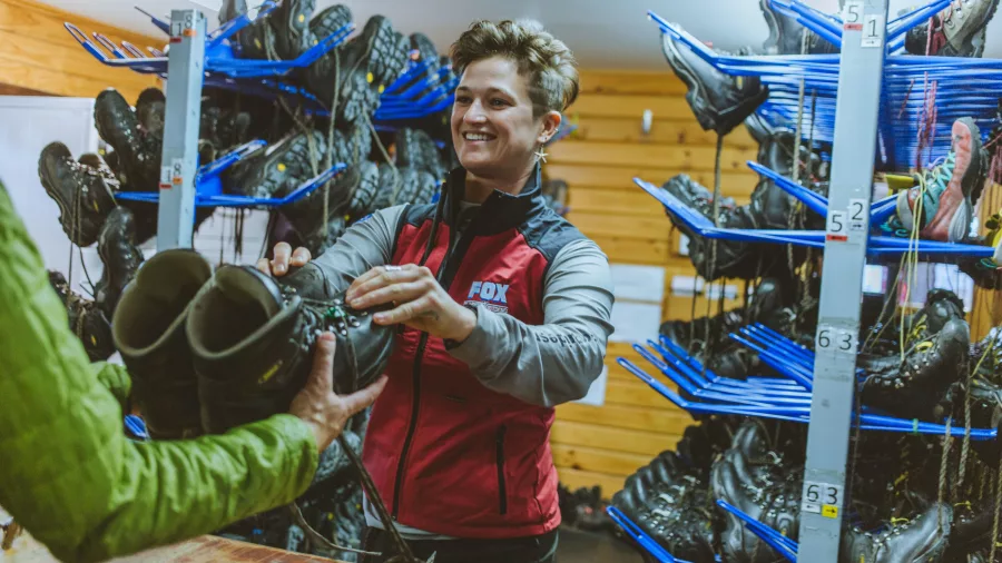 A staff member hands out hiking boots inside the Fox Glacier gear room.