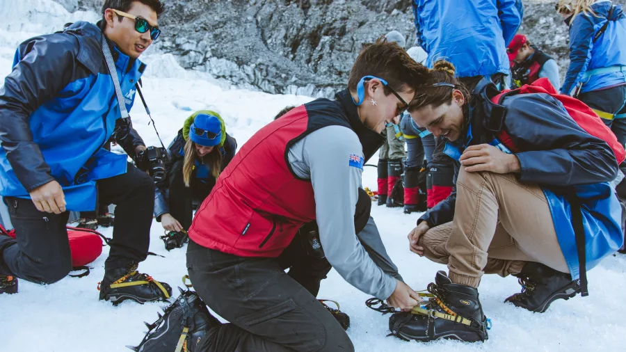 A guide helps fit crampons onto a guest's boots on the glacier ice.