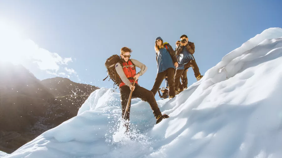 A guide demonstrates ice axe techniques on a slope while hikers look on.