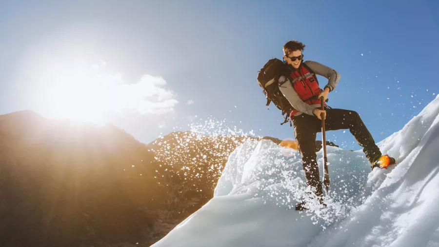 A glacier guide uses an ice axe on a steep slope under bright sunshine.