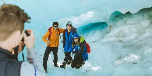 A group poses inside an ice cave while another guest takes a photo.