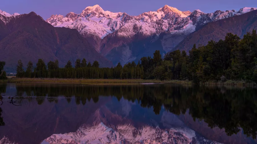 Sunset light on Aoraki / Mount Cook and the Southern Alps reflected in the still waters of Lake Matheson near Franz Josef