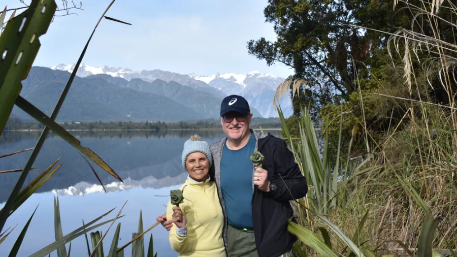 Couple holding flax flowers by Lake Mapourika with Southern Alps in background