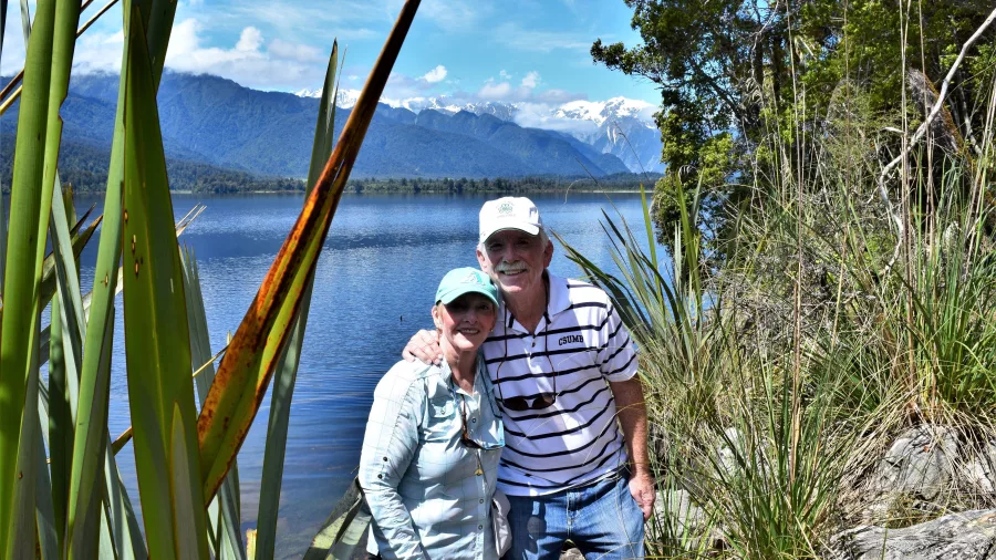 Couple smiling together beside Lake Mapourika with snowy mountains in the background