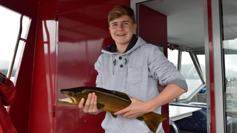 Teen boy holding a freshly caught brown trout on a Lake Mapourika fishing boat