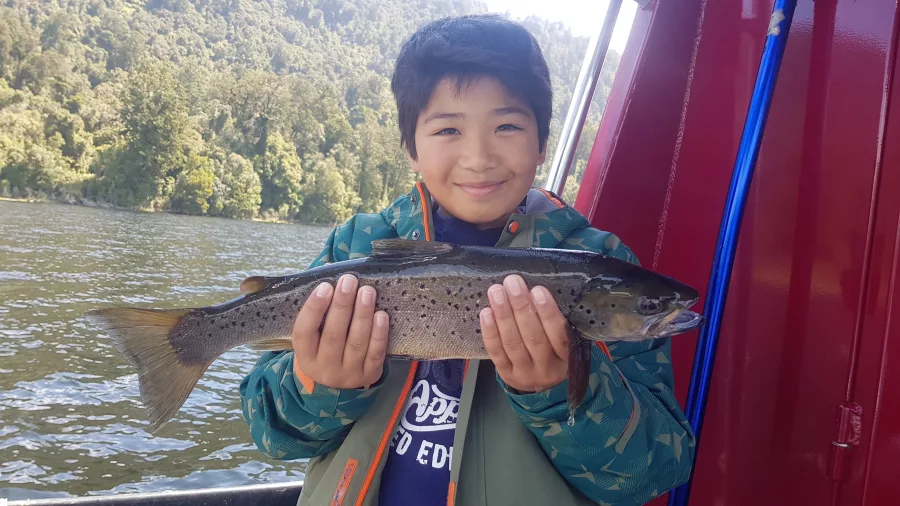 Young boy proudly holding a freshly caught brown trout during a fishing trip in Franz Josef, New Zealand