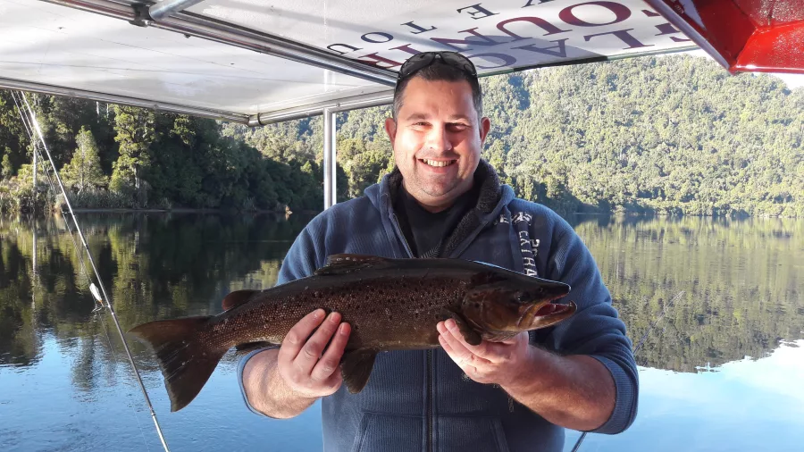 Man smiling and holding a large brown trout caught during a fishing tour in Franz Josef, New Zealand