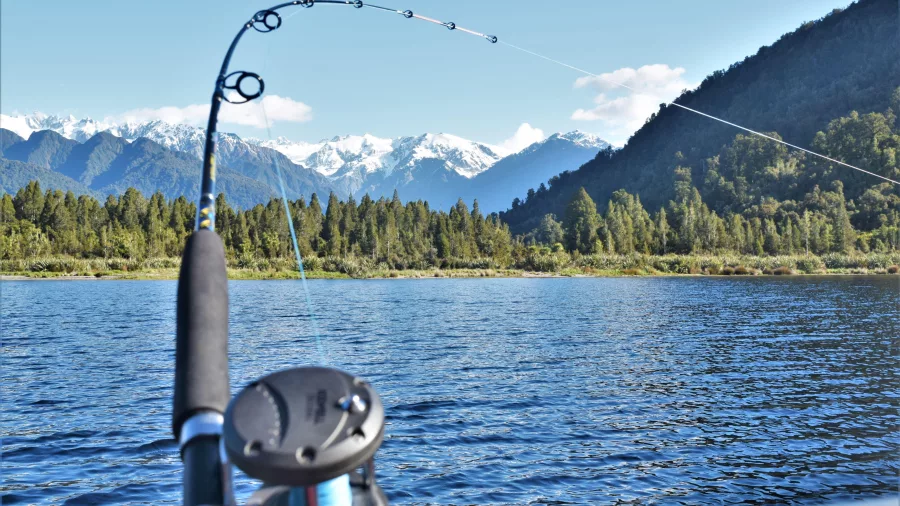 Fishing rod bent over Lake Mapourika with Southern Alps in the background