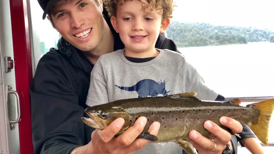 Smiling man and child holding a freshly caught fish on Lake Mapourika