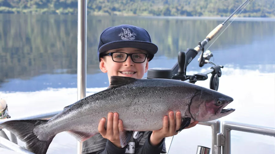 Smiling young boy holding a freshly caught salmon during a Franz Josef fishing trip