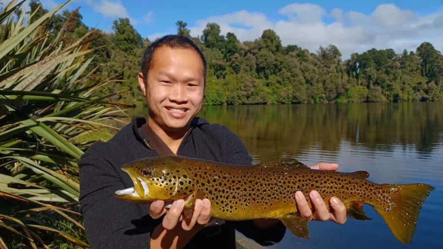 Angler smiling while holding a freshly caught brown trout at Lake Mapourika