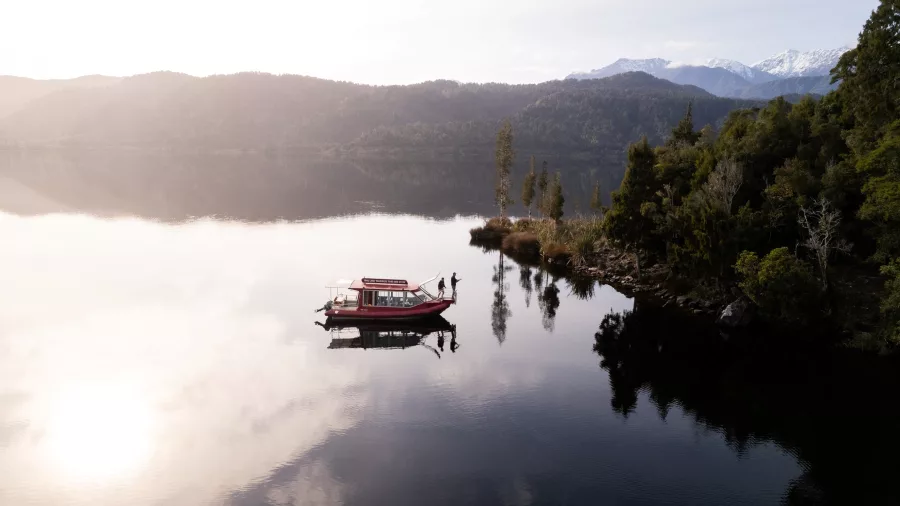 Scenic fishing tour boat on Lake Mapourika with early morning reflections and mountain backdrop