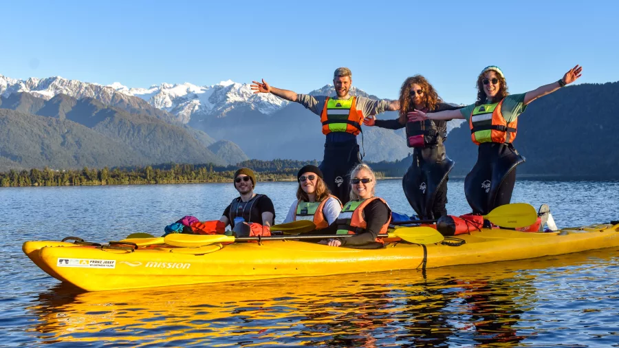 Group of people in yellow kayaks posing on a lake with snow-capped mountains in the background