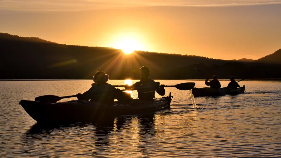 Silhouettes of kayakers paddling across Lake Mapourika during sunset near Franz Josef.