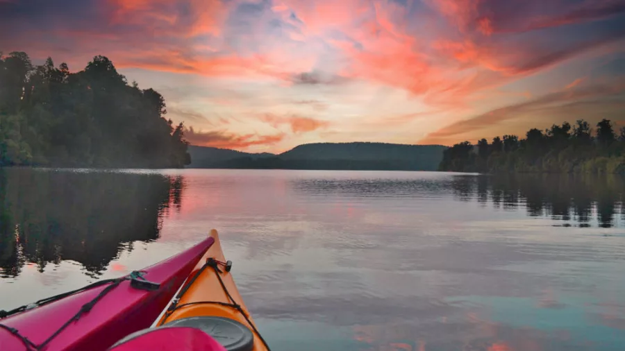 View from a kayak on Lake Mapourika at sunset with vivid pink and orange clouds reflecting on the water.