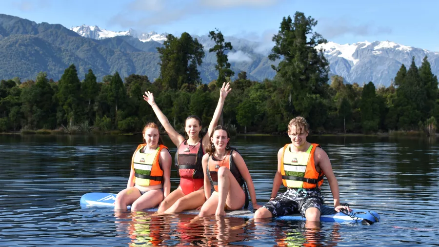 Group paddleboarding on Lake Mapourika with snow-capped Southern Alps in the background