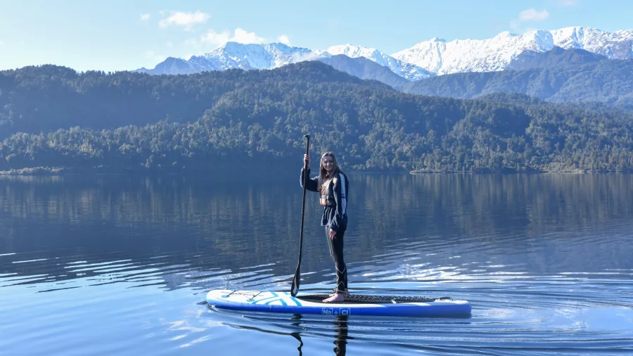 Woman paddleboarding alone on Lake Mapourika with snowy Southern Alps in the background