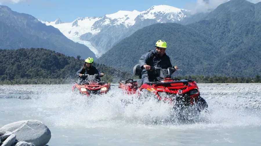 Two riders splash through a shallow river on quad bikes near Franz Josef Glacier on New Zealand’s West Coast