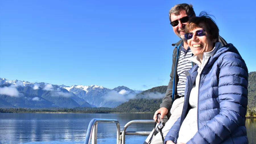 Smiling couple enjoying a scenic cruise on Lake Mapourika with snow-capped mountains in the background