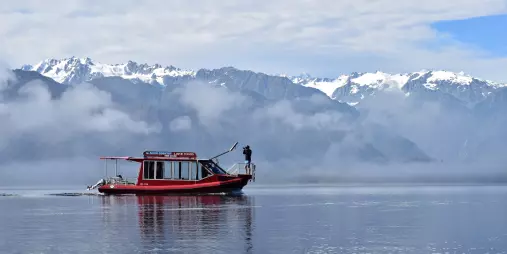 Scenic cruise boat on Lake Mapourika with snow-capped Southern Alps in the background, Franz Josef