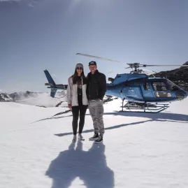 Couple standing in front of Glacier Country Helicopters on a snowy landing in Franz Josef