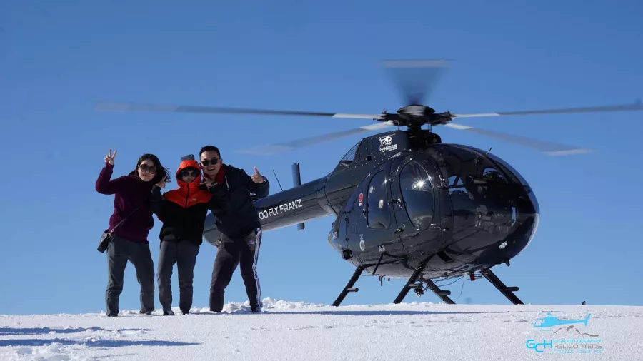 Group posing beside Glacier Country Helicopters MD520N after snow landing in Franz Josef