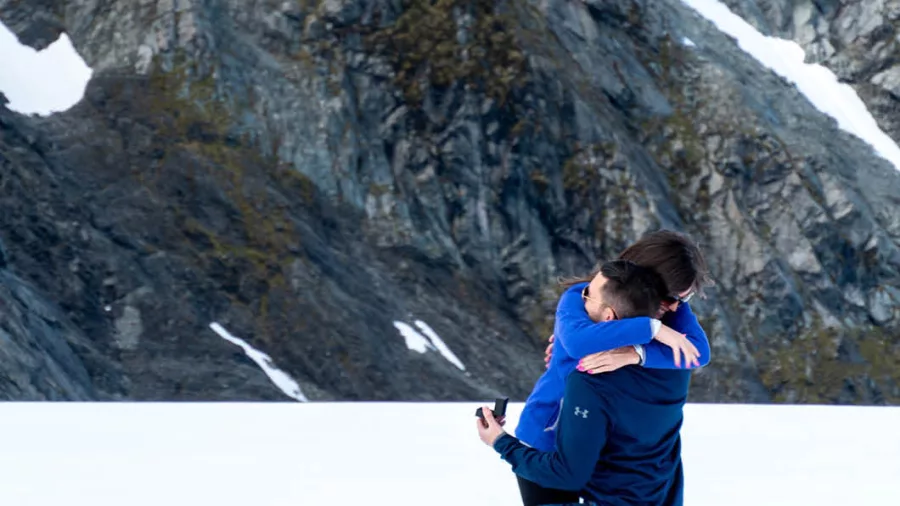 Couple embracing on a snowy glacier after a helicopter proposal with Glacier Country Helicopters