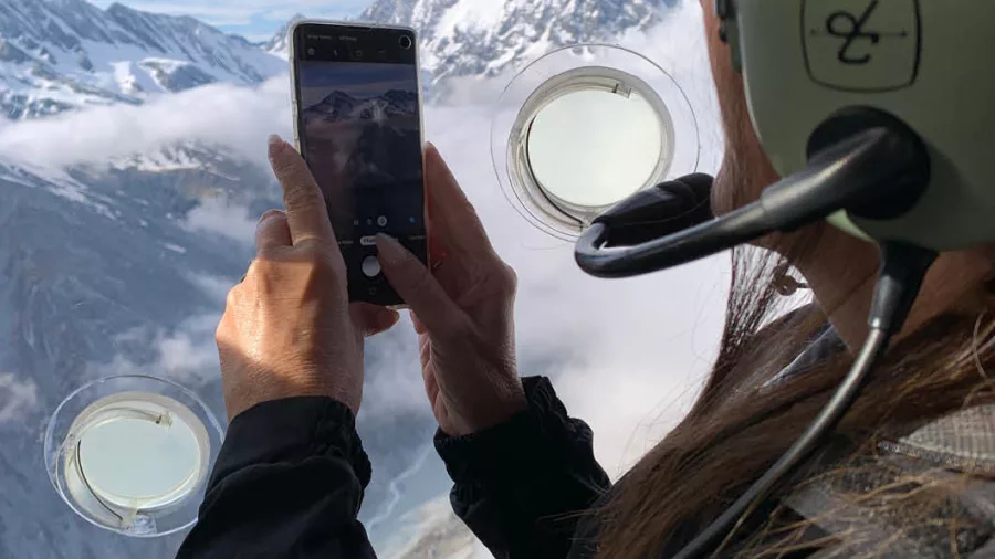 Passenger taking photo of snow-capped mountains through Glacier Country Helicopters window