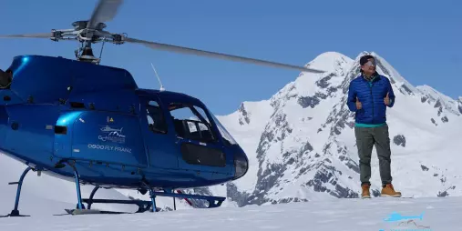 Man standing beside Glacier Country Helicopters AS350 with snow-covered Southern Alps in the background