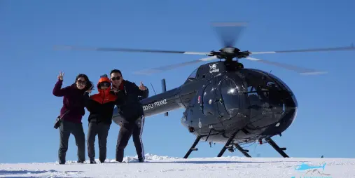 Group posing beside Glacier Country Helicopters MD520N after snow landing in Franz Josef