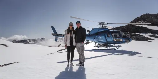 Couple standing in front of Glacier Country Helicopters on a snowy landing in Franz Josef