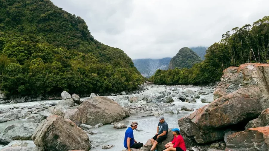 Small group sitting on rocks beside glacial river in Fox Glacier Valley