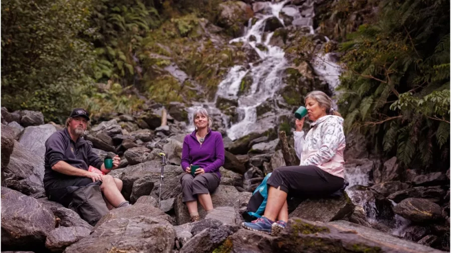 Three hikers resting by a waterfall in Franz Josef forest