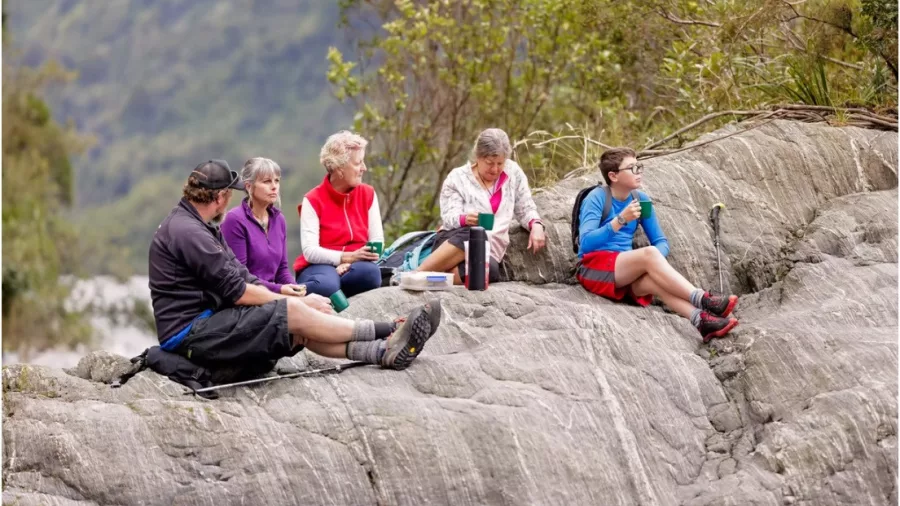 Group sitting on a rocky surface enjoying a picnic during Franz Josef tour