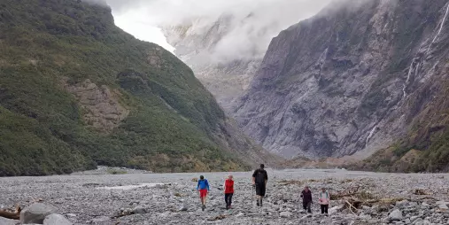 Group of walkers crossing the Franz Josef Glacier valley floor under dramatic cloud cover