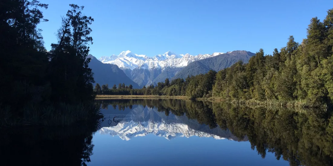Lake Matheson reflection of snow-capped mountains in clear blue sky