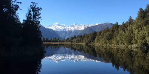Lake Matheson reflection of snow-capped mountains in clear blue sky