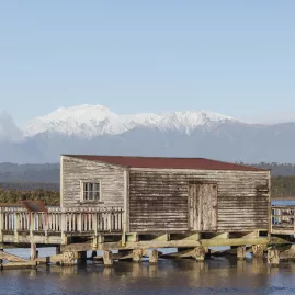 Historic Okarito boathouse with snow-covered Southern Alps in the background, West Coast New Zealand