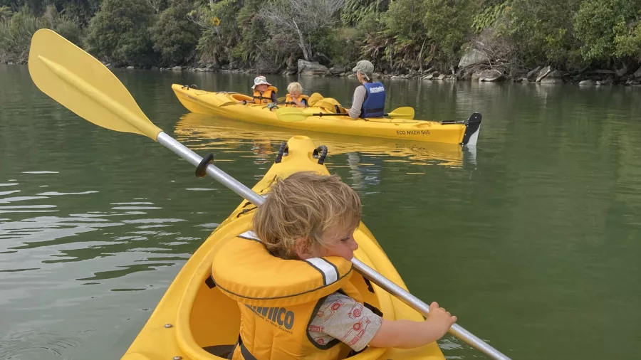 Young child in a yellow kayak enjoying a family-friendly eco tour at Ōkārito Lagoon, West Coast New Zealand