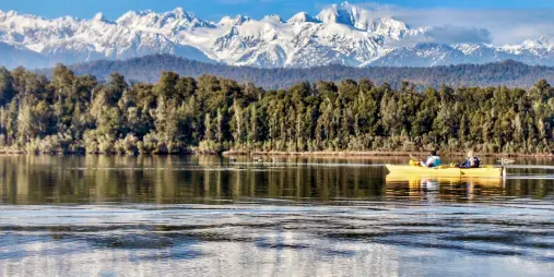 Kayakers paddling on Okarito Lagoon with snow-covered Southern Alps in the background