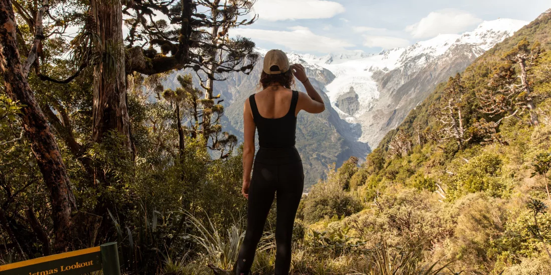 Woman standing at a scenic viewpoint on the Alex Knob Track looking towards the Franz Josef Glacier in Westland Tai Poutini National Park