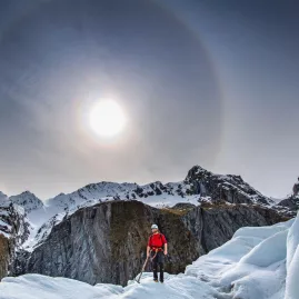 Person helihiking on Fox Glacier under a bright sun halo in the Southern Alps