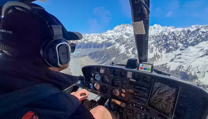 Helicopter pilot flying over snow-covered Franz and Fox Glaciers in New Zealand