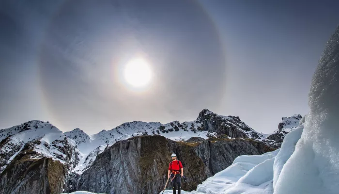 Person helihiking on Fox Glacier under a bright sun halo in the Southern Alps