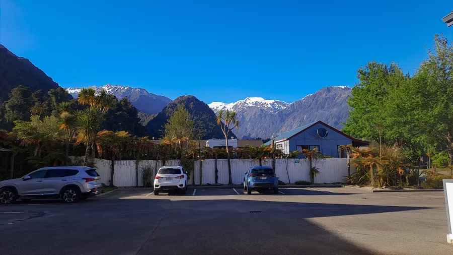 Snow-capped Southern Alps rising behind Franz Josef Village under a clear blue sky
